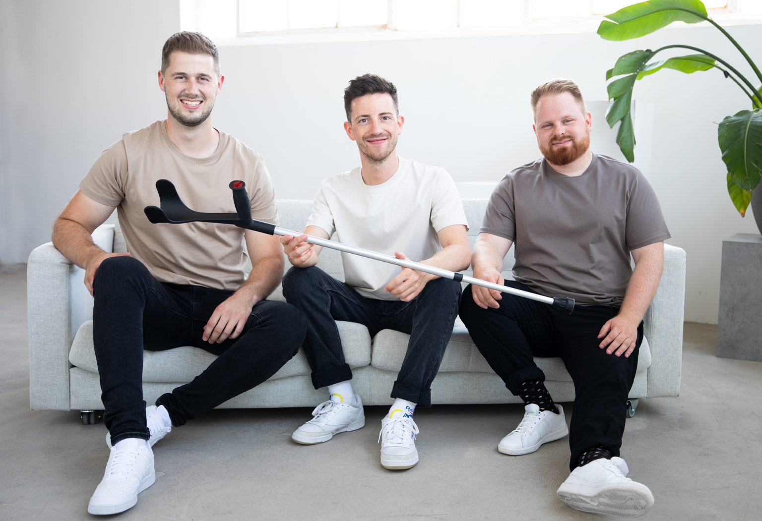 Die drei Gründer von Steets, Thorben Engel, Phil Janßen und Philipp Battisti sitzen auf einem Sofa und halten eine Krücke in der Hand.